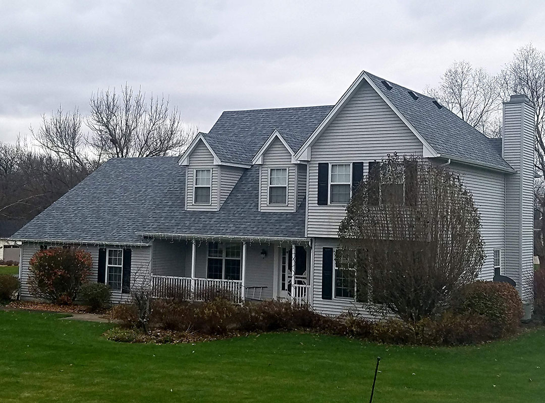 A house with a gray roof in the middle of a grassy field.