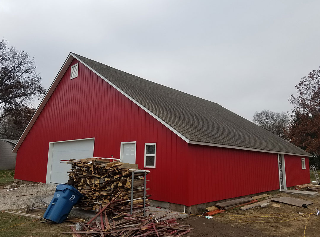 A red barn with many wood stacked on top of it.