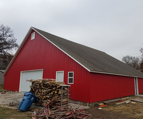 A red barn with many wood stacked on top of it.