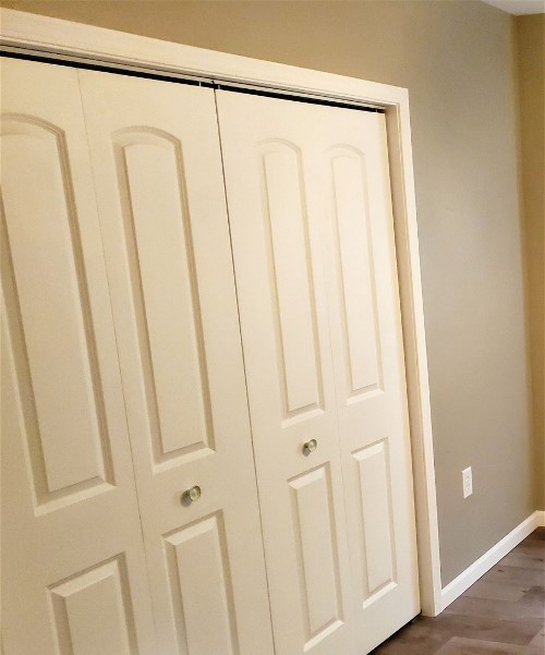 A room with white closet doors and hardwood floors.