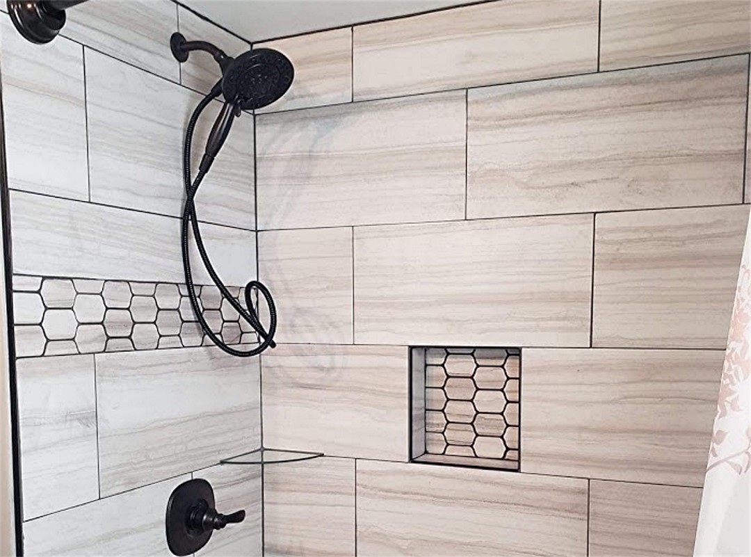 A shower with white tile and black shower head.