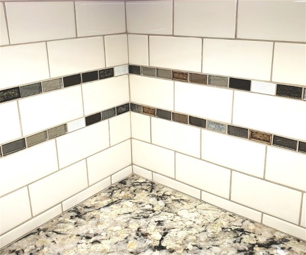 A corner of a tiled bathroom with white walls and black and silver tiles.