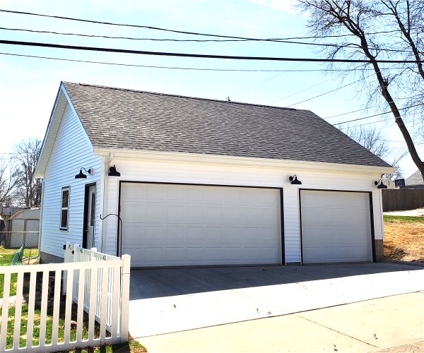 A white two car garage with a fence and trees.