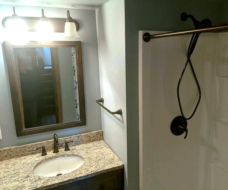 A bathroom with a sink, mirror and shower.