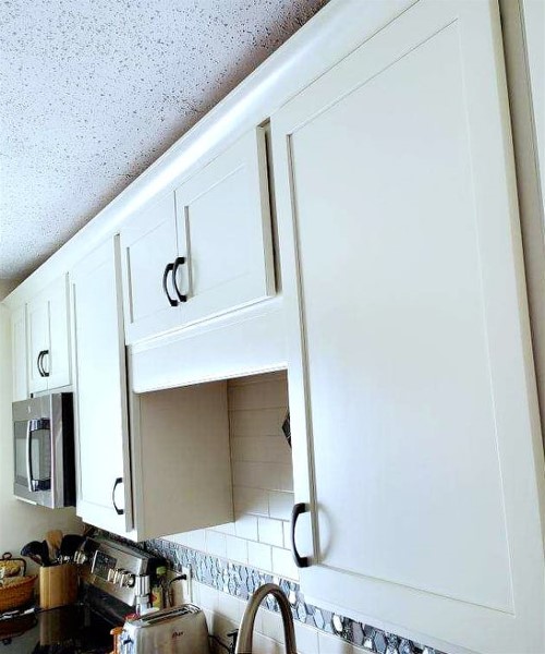 A kitchen with white cabinets and black handles.