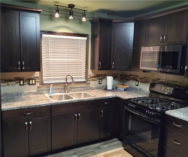 A kitchen with dark cabinets and white counters.