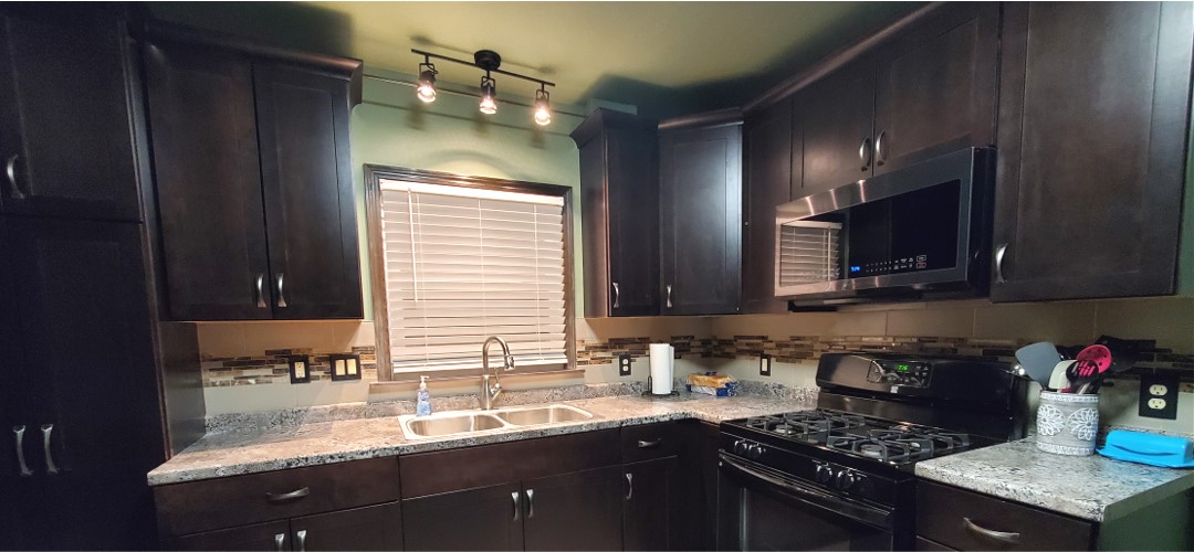 A kitchen with dark cabinets and white counters.