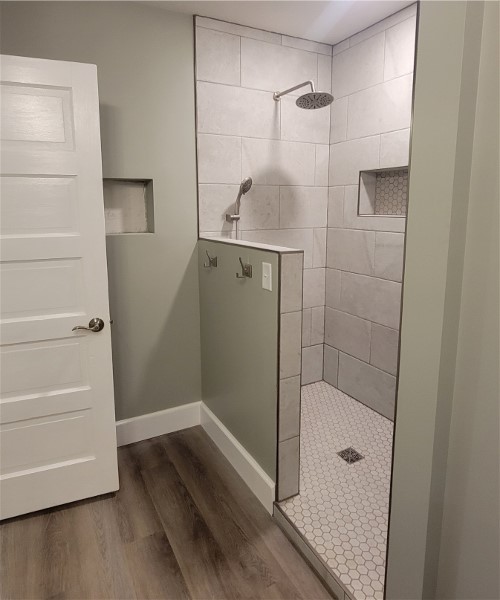 A bathroom with a walk in shower and wood flooring.