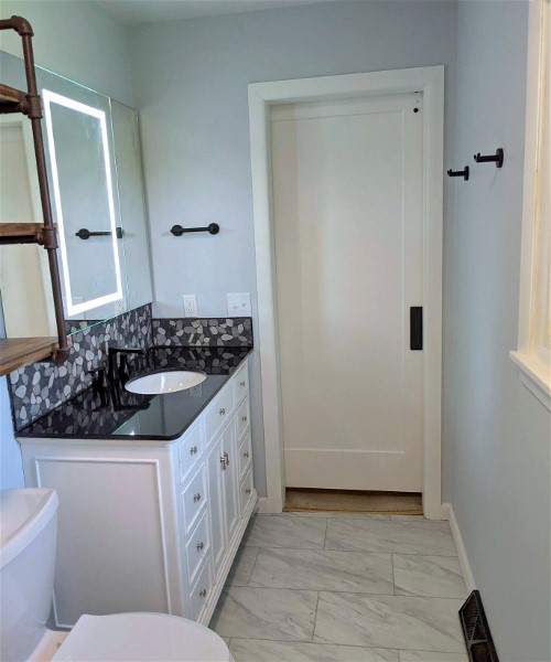 A bathroom with white cabinets and black counter tops.