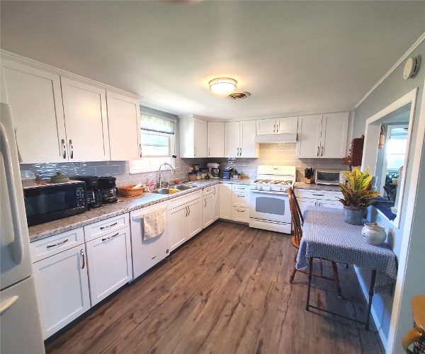 A kitchen with white cabinets and wooden floors.