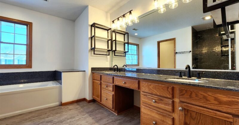 A bathroom with wooden cabinets and floors, a tub and sink.